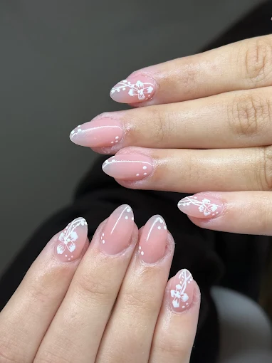 Two hands with almond shaped BIAB nails in a soft pink, painted with fine white florals and dots.