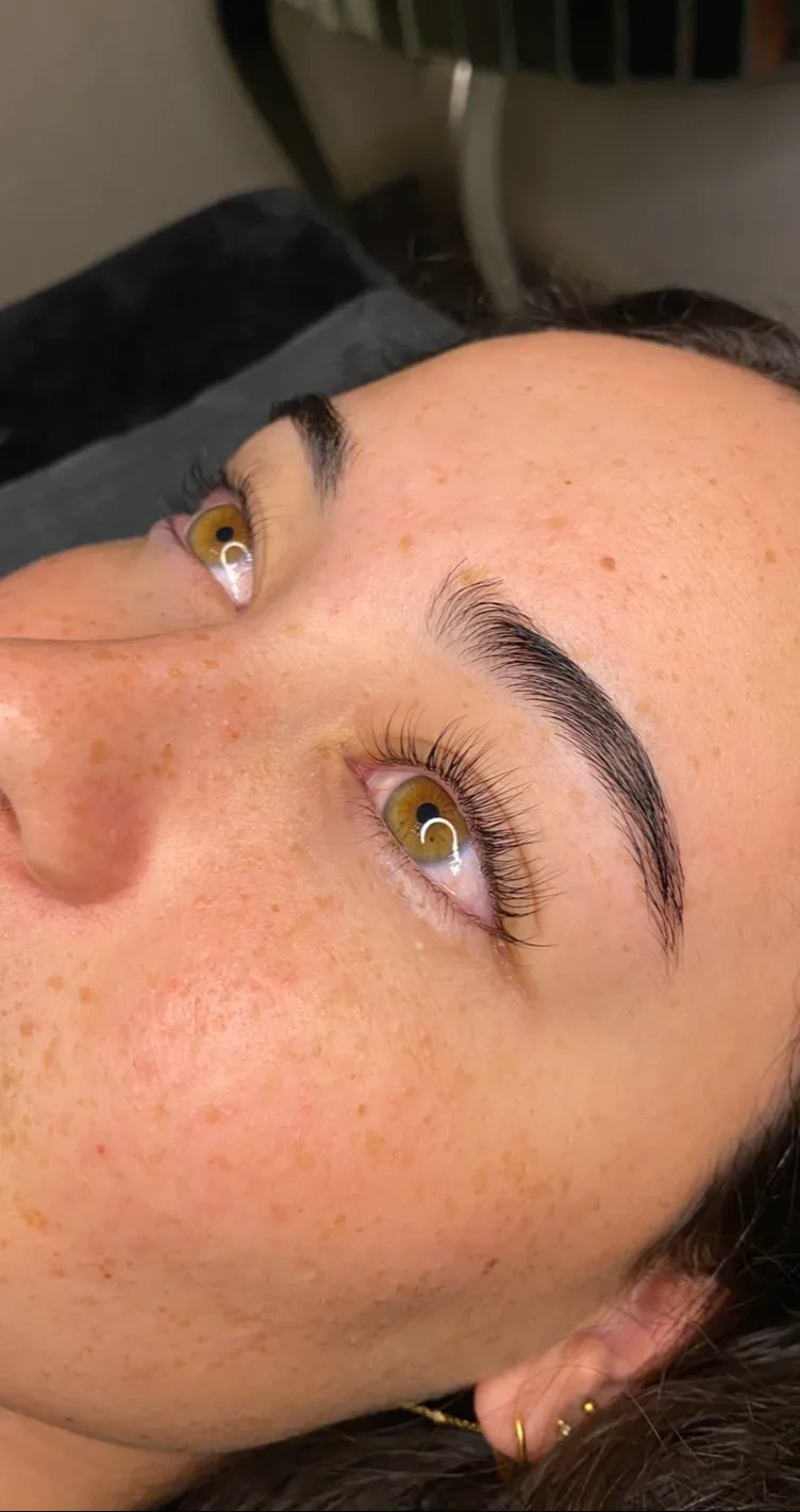 A client on the treatment bed, brows laminated and brushed upward, lashes lifted.