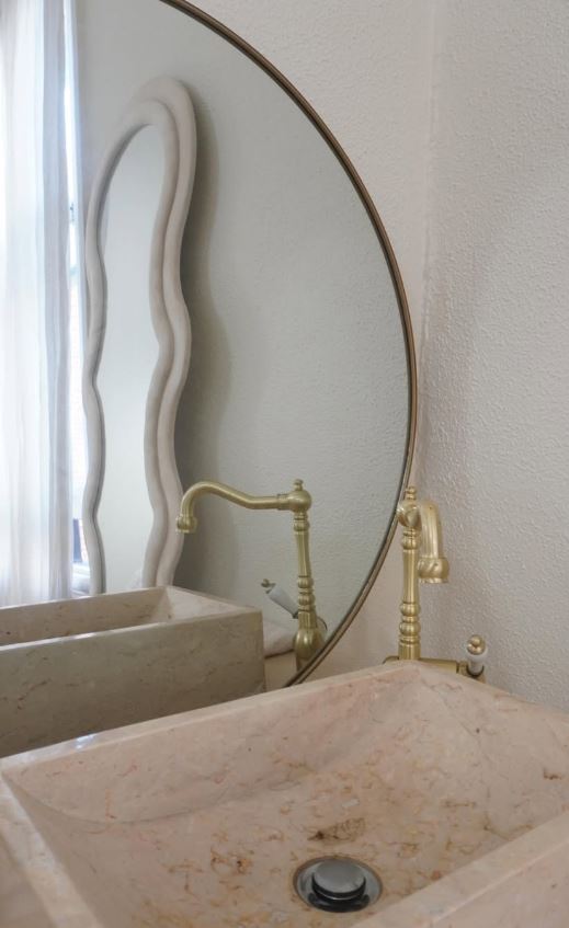 A pink marble basin with brass tapware, below a round brass framed mirror.